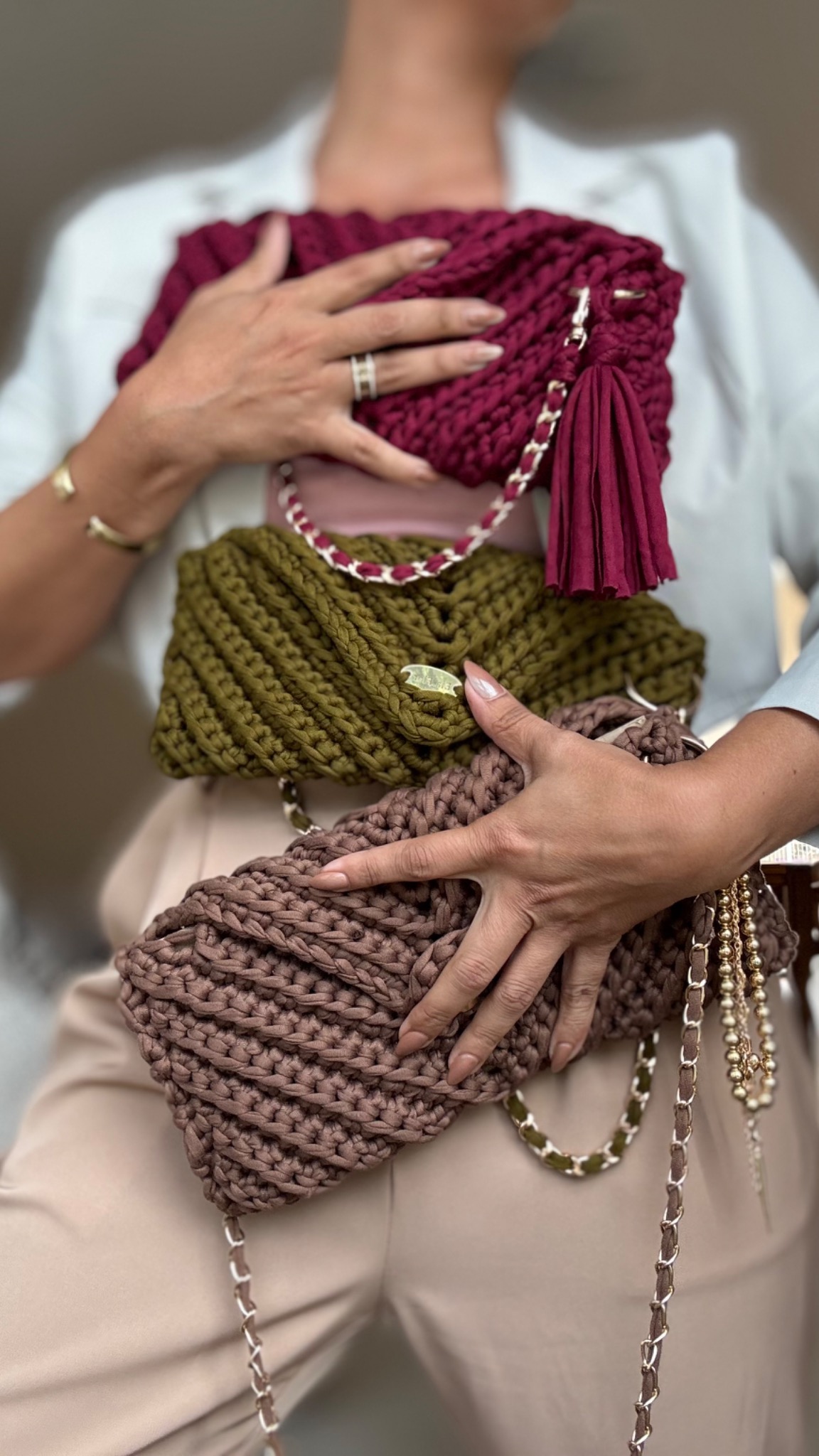 Ela Flor maker holding four handmade crochet bags in burgundy, olive and neutral tones